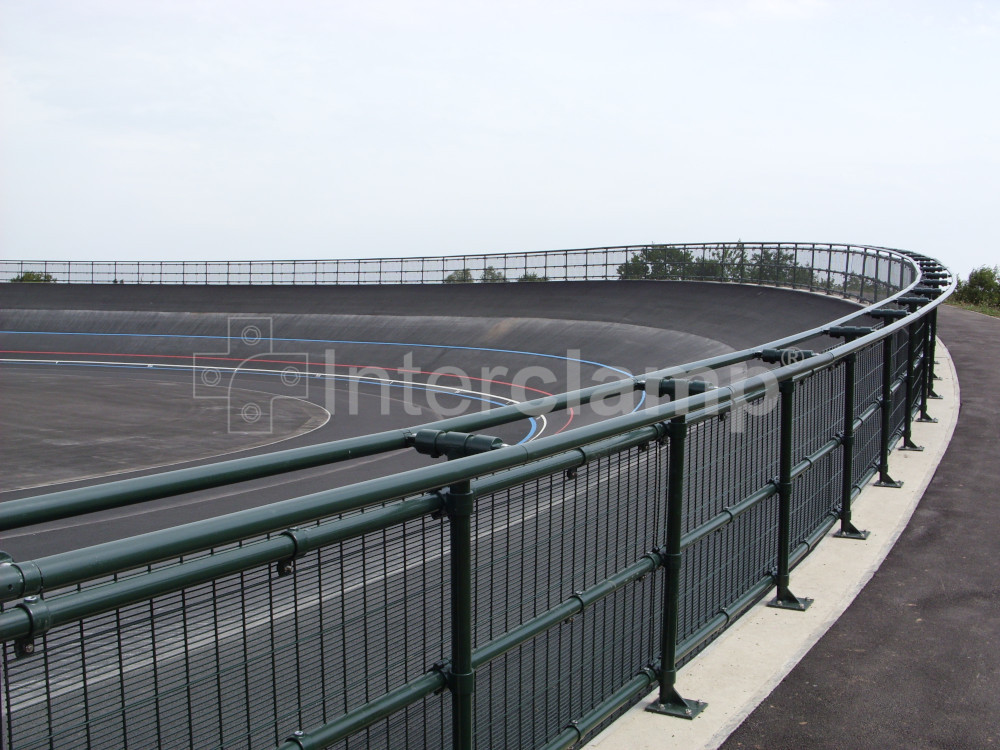 Dark green powder-coated Interclamp key clamp DDA fittings creating a sturdy safety barrier along the track of a velodrome, blending seamlessly with the surroundings.